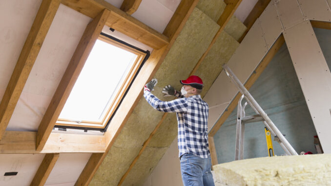 Man installing thermal roof insulation layer  - using mineral wool panels. Attic renovation and insulation concept